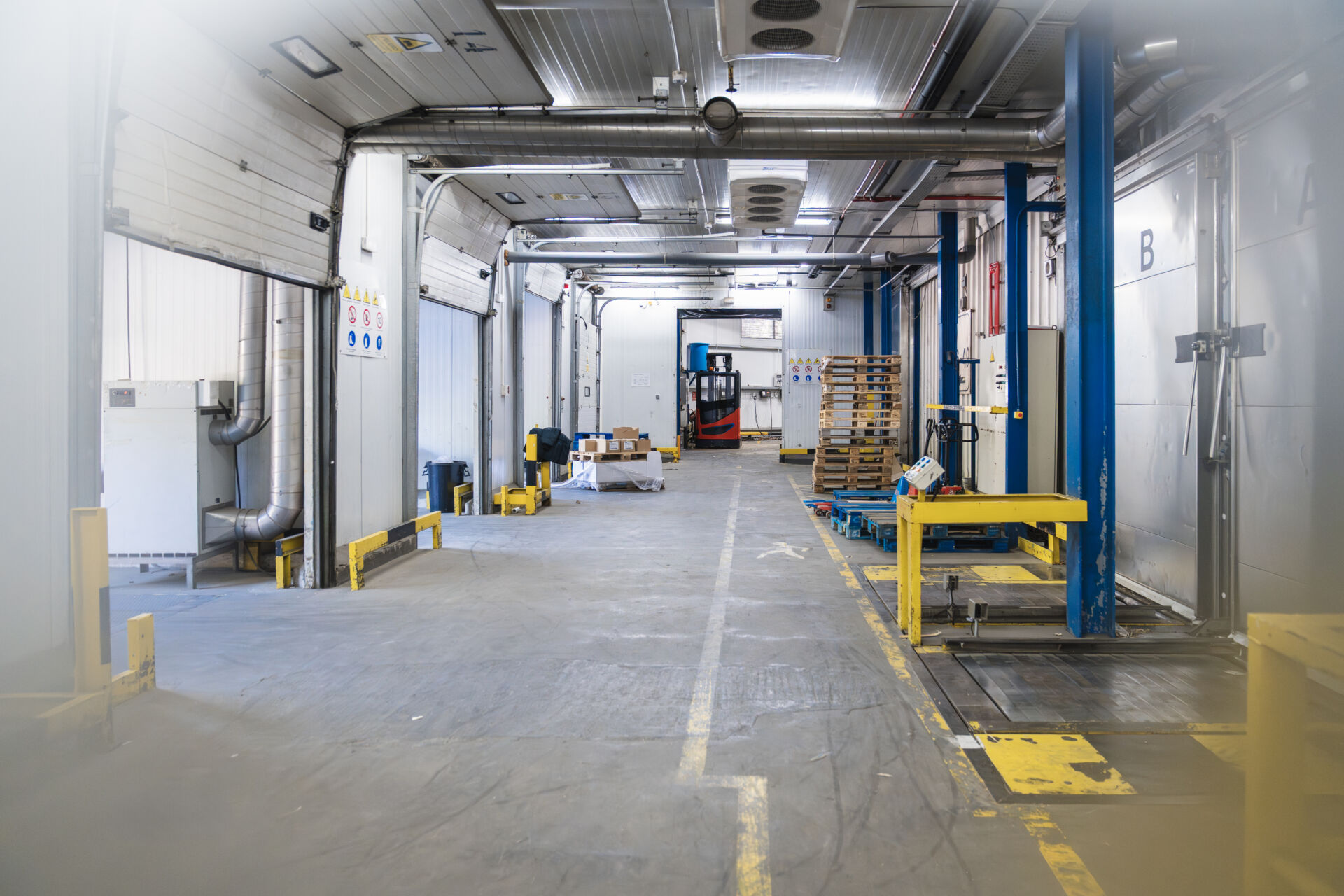 Coldcase cold storage warehouse loading area with commercial refrigeration pipework, pallets and a forklift
